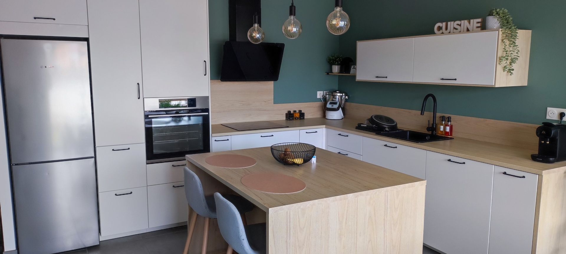 Cuisine moderne avec armoires blanches, réfrigérateur en acier inoxydable et mur d'accent turquoise.