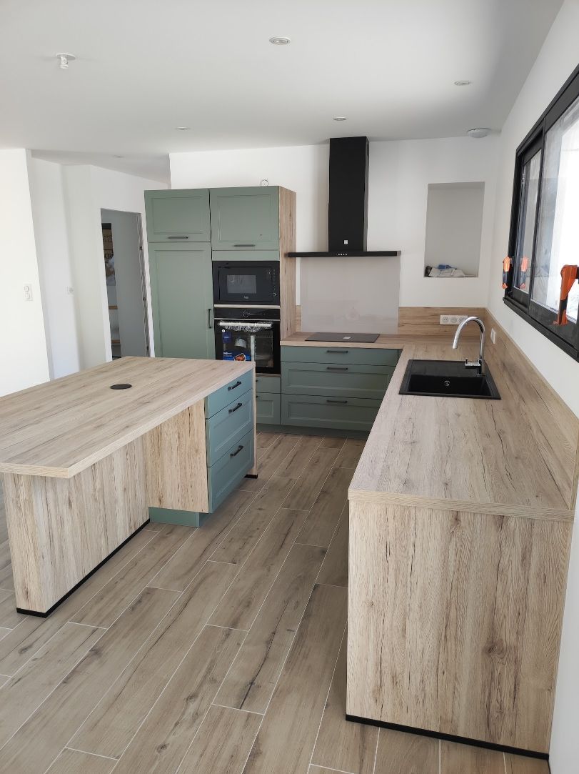 Cuisine moderne avec des armoires en bois clair, des touches de vert sauge et une hotte noire.