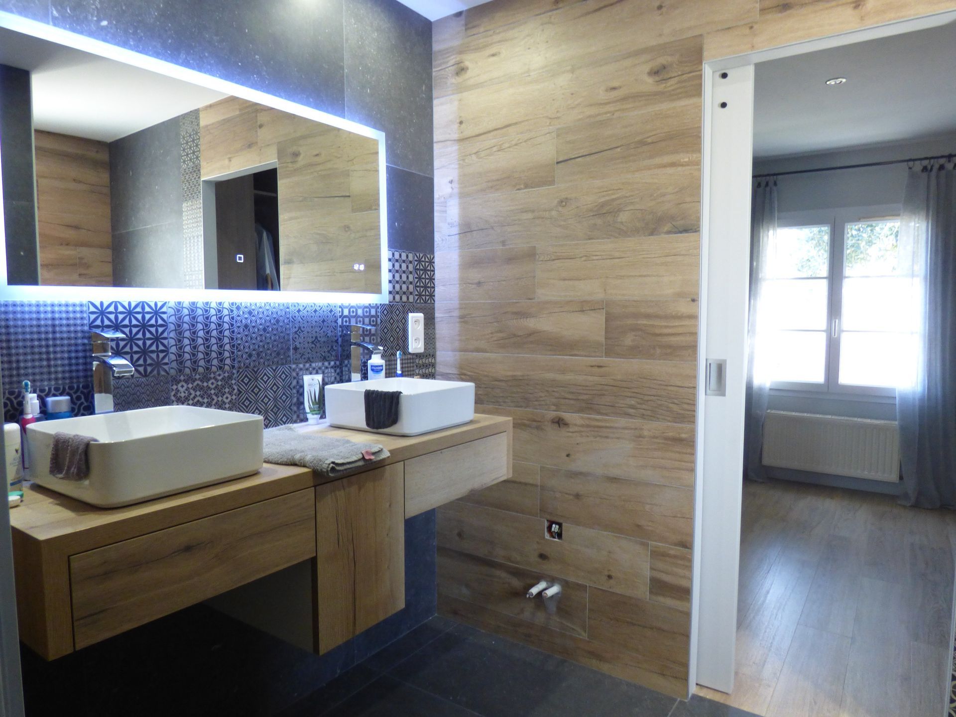 Salle de bains moderne avec boiseries, meuble-lavabo suspendu, vasques rectangulaires et miroir éclairé. 