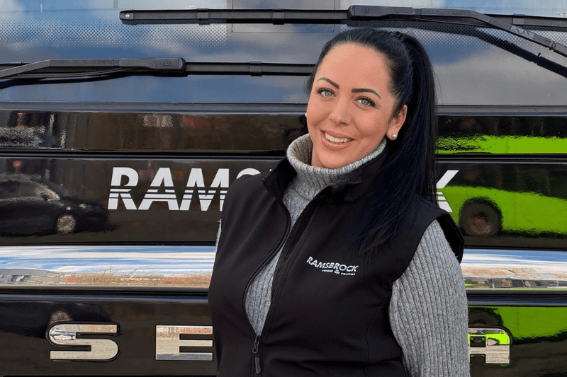 Eine Frau steht vor einem Bus und lächelt.