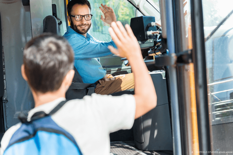 Ein Mann winkt einem Busfahrer zu, während er auf dem Fahrersitz sitzt.
