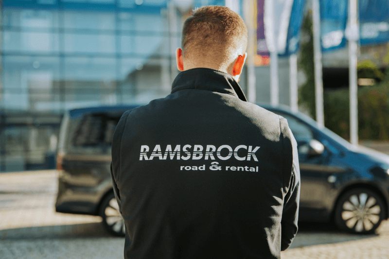 Ein Mann in einer Ramsbrock Road- und Rent-Jacke steht vor einem Auto.