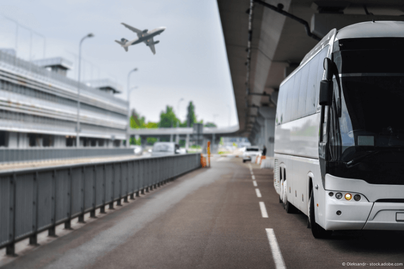 Ein Bus von Ramsbrock Road & Rentals Shuttleservice in Frankfurt fährt eine Straße entlang, im Hintergrund fliegt ein Flugzeug.