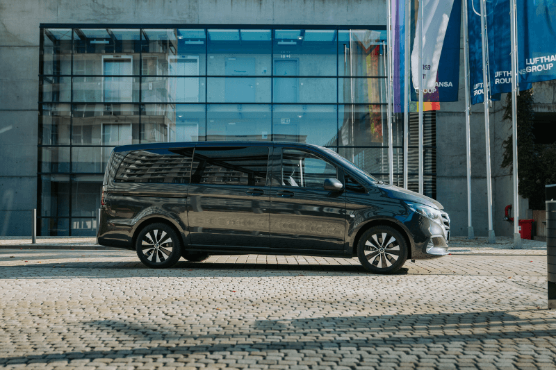 Ein schwarzer Lieferwagen parkt auf einer Kopfsteinpflasterstraße vor einem Gebäude.