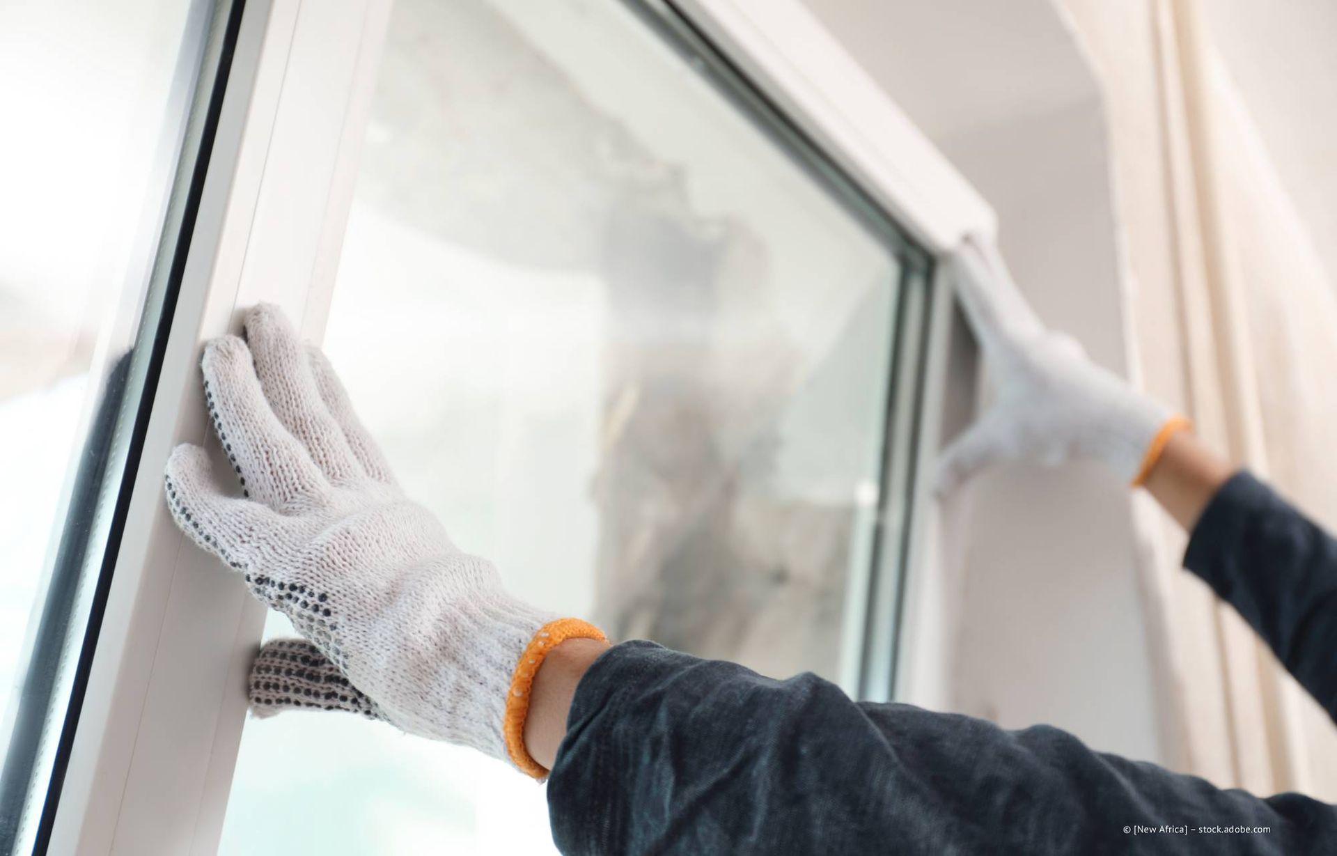 Hände in Arbeitshandschuhen montieren einen Fensterrahmen.
