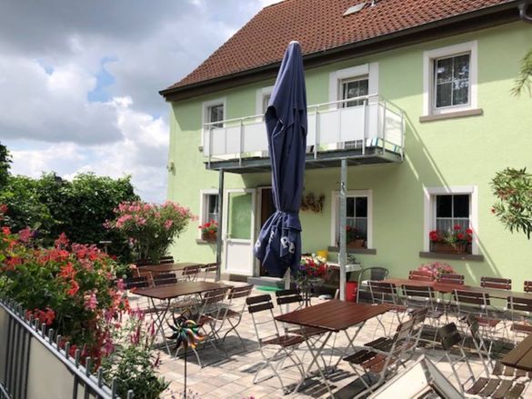 A patio with tables and chairs and an umbrella in front of a green building.