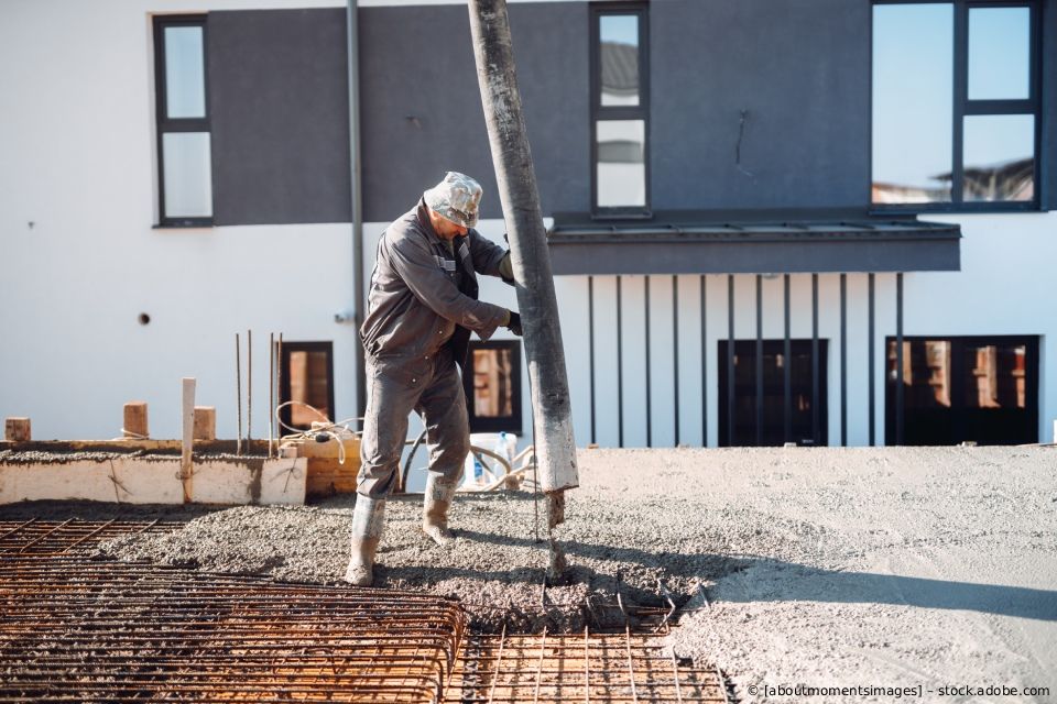 Ein Bauarbeiter führt einen Betonschlauch, um nassen Beton auf ein Stahlbewehrungsgitter auf einer Baustelle zu gießen.