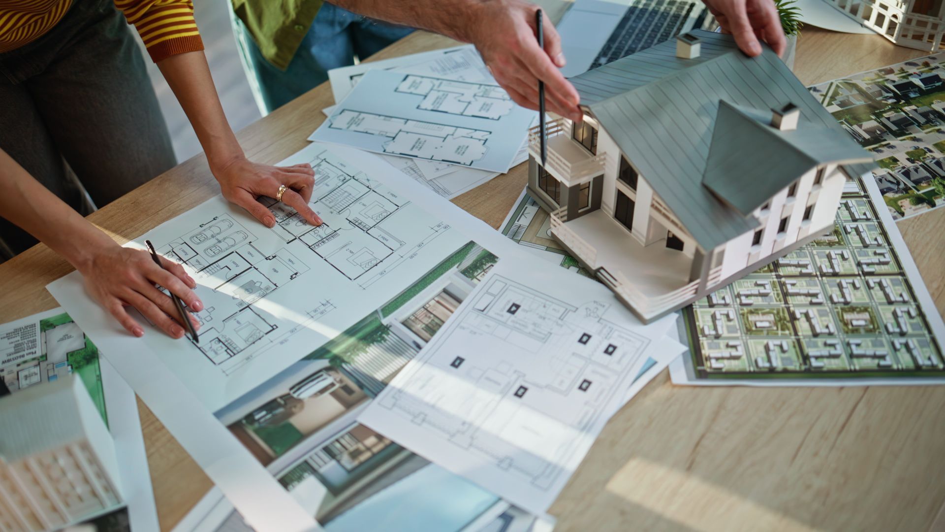 Des personnes examinent des plans architecturaux à côté d'une maquette de maison posée sur une table.