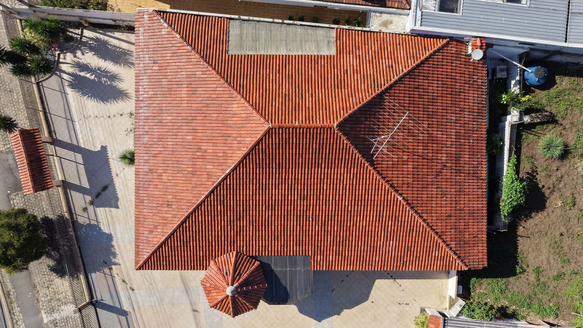 Vue aérienne d'une maison au toit de tuiles rouges avec un petit patio, une allée et un petit jardin.
