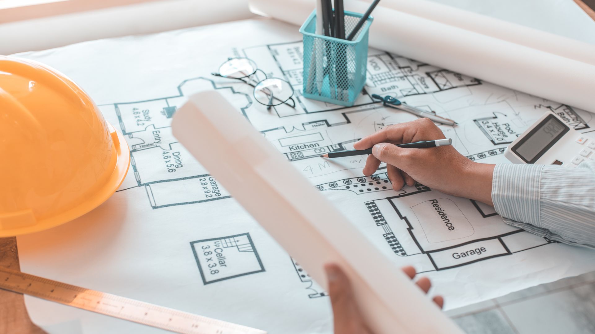Plans architecturaux dessinés à la main, à côté d'un casque de chantier orange et d'une règle.