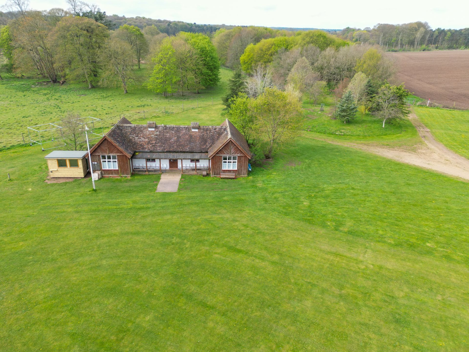 Une petite ferme rouge sur une colline verdoyante, avec des arbres et des champs en arrière-plan.