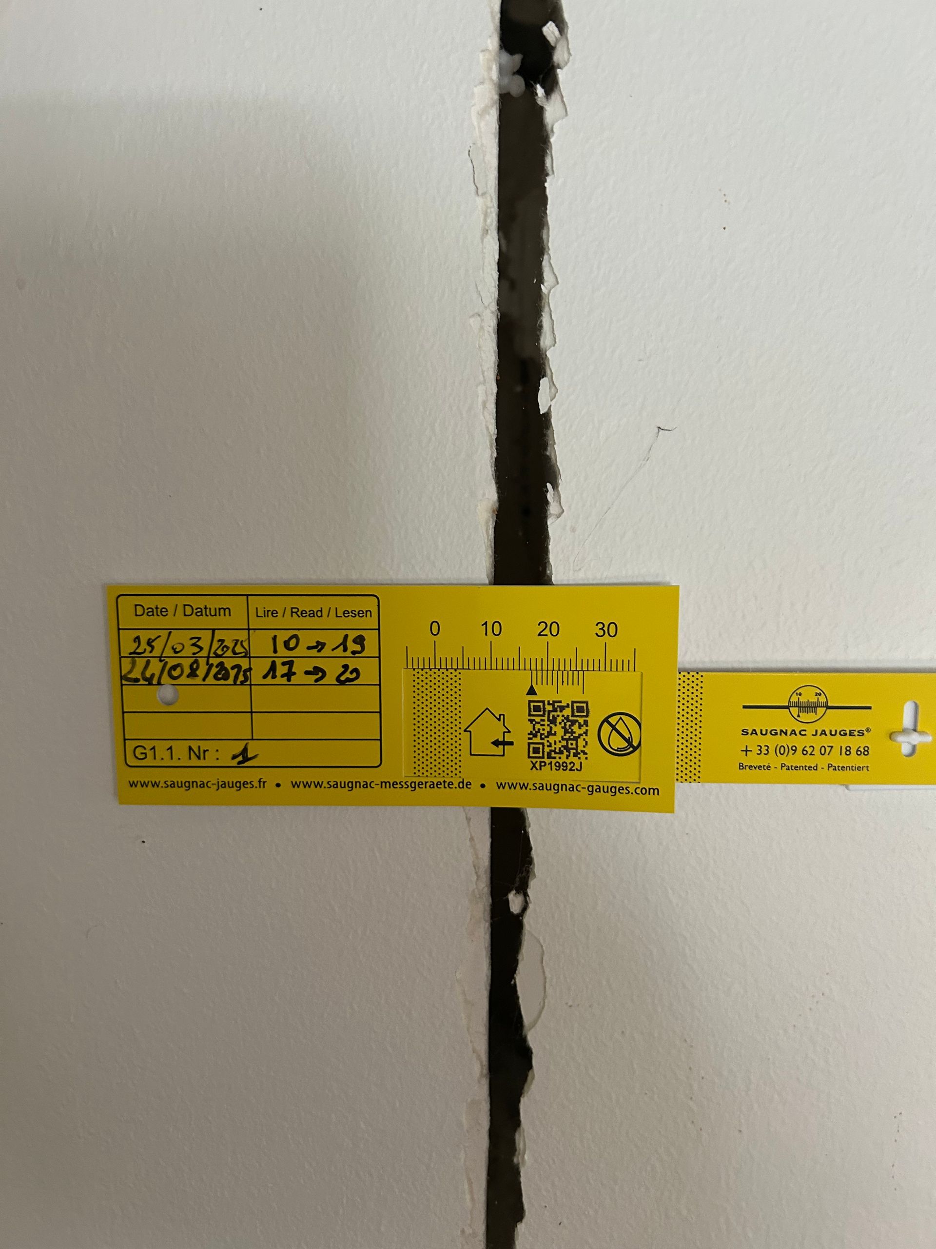 Étiquettes d'inspection jaunes signalant une fissure verticale dans un mur blanc.