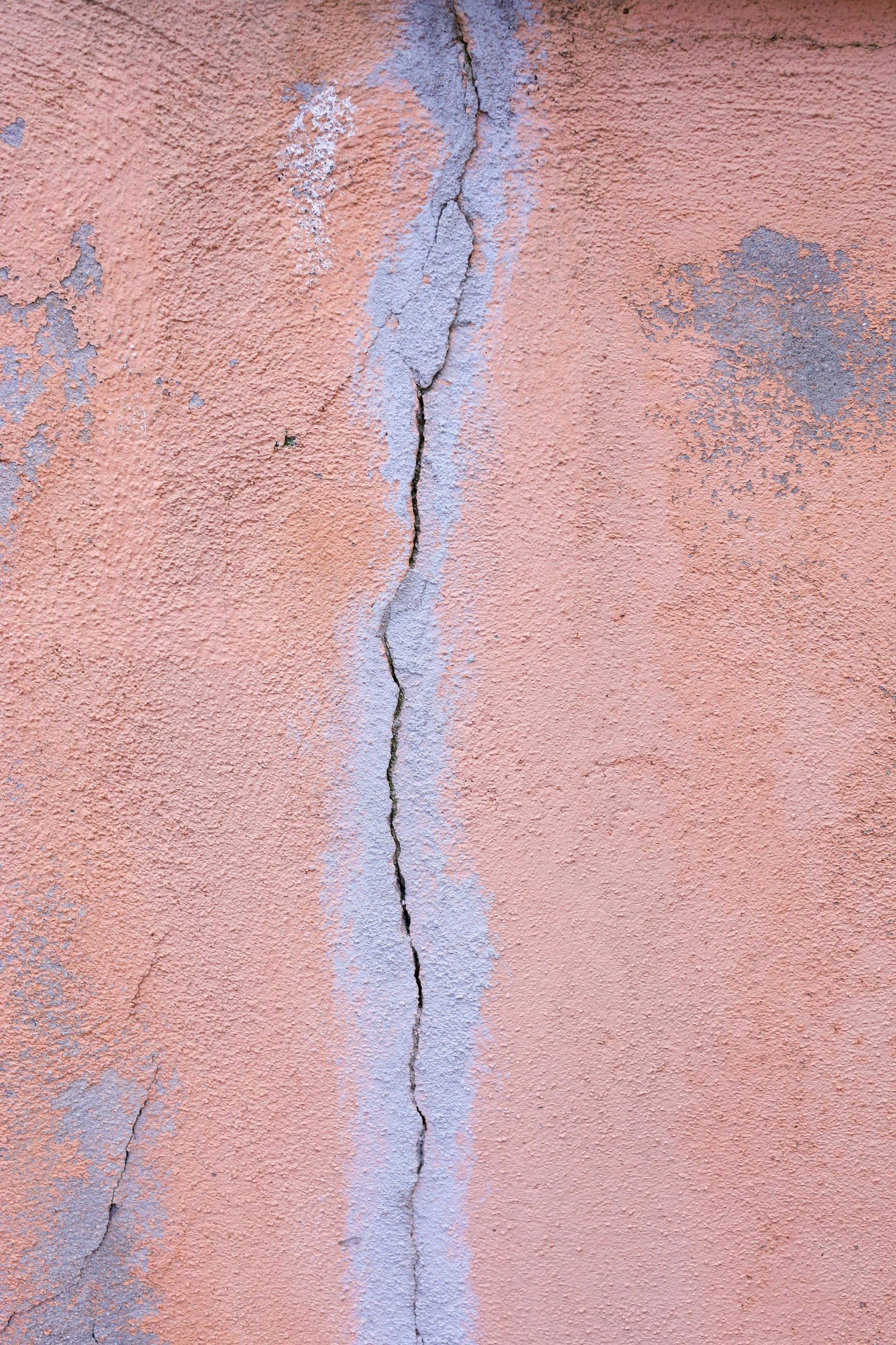 Gros plan sur un mur en stuc rose présentant une fissure verticale bleu-gris.