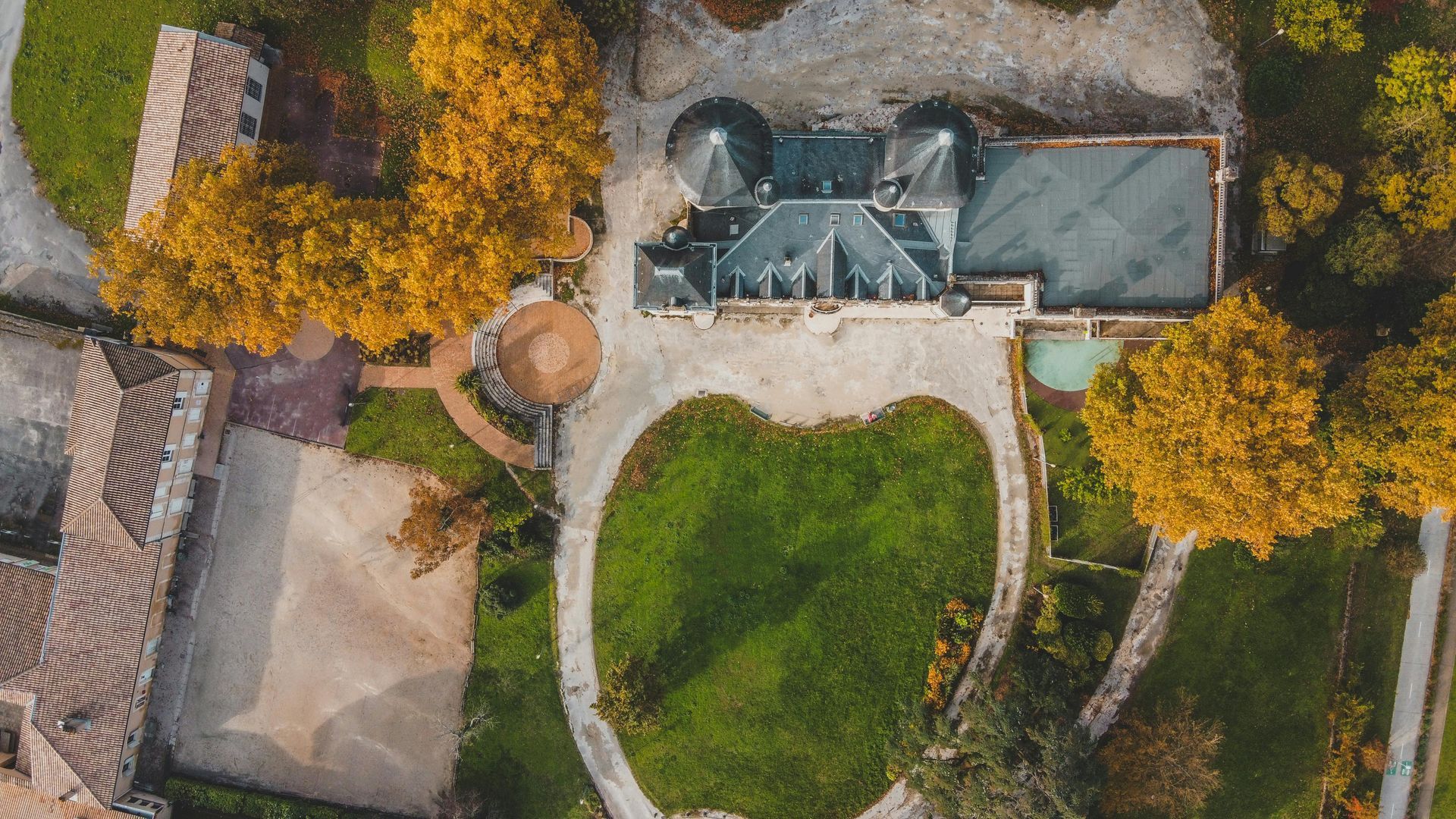 Vue aérienne d'une maison entourée d'une pelouse verte, de chemins de pierre et d'arbres aux couleurs d'automne.