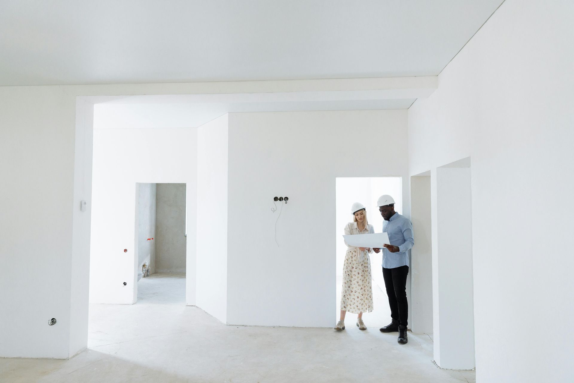 Deux personnes portant des casques de chantier discutent de projets dans une pièce blanche lumineuse en travaux.