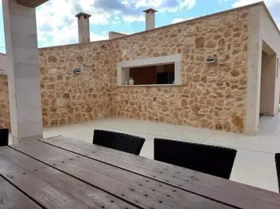Patio con pared de piedra, mesa y sillas de madera.