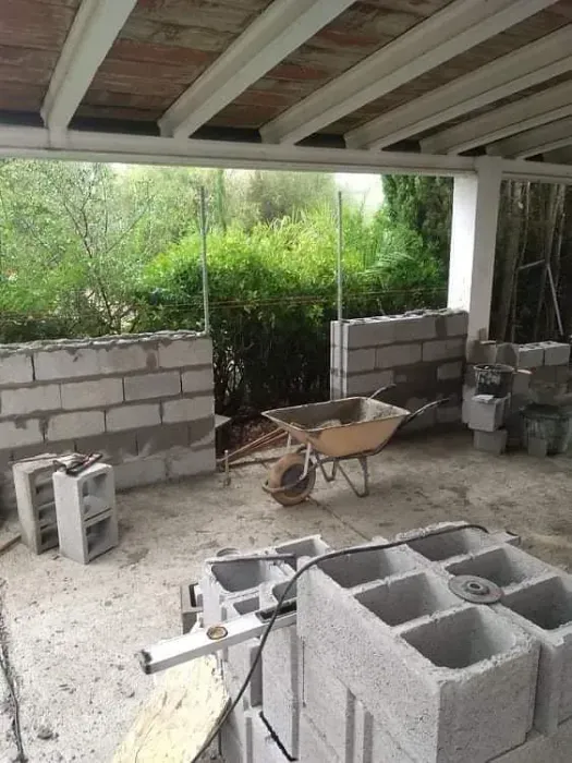 Sitio de construcción: se construyen paredes de bloques de hormigón con una carretilla, una sierra y bloques visibles.