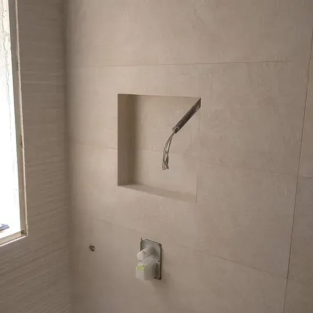 Pared de baño con nicho alicatado y grifería de ducha.