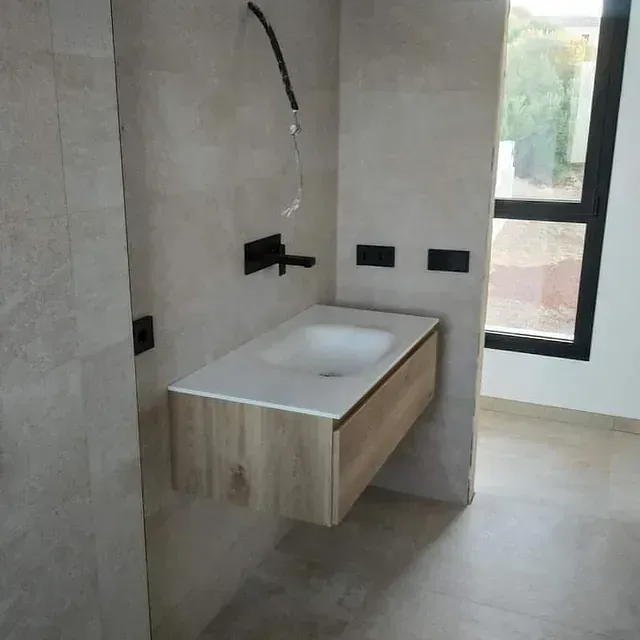 Tocador de baño de madera flotante con lavabo blanco sobre una pared de azulejos de color beige claro.
