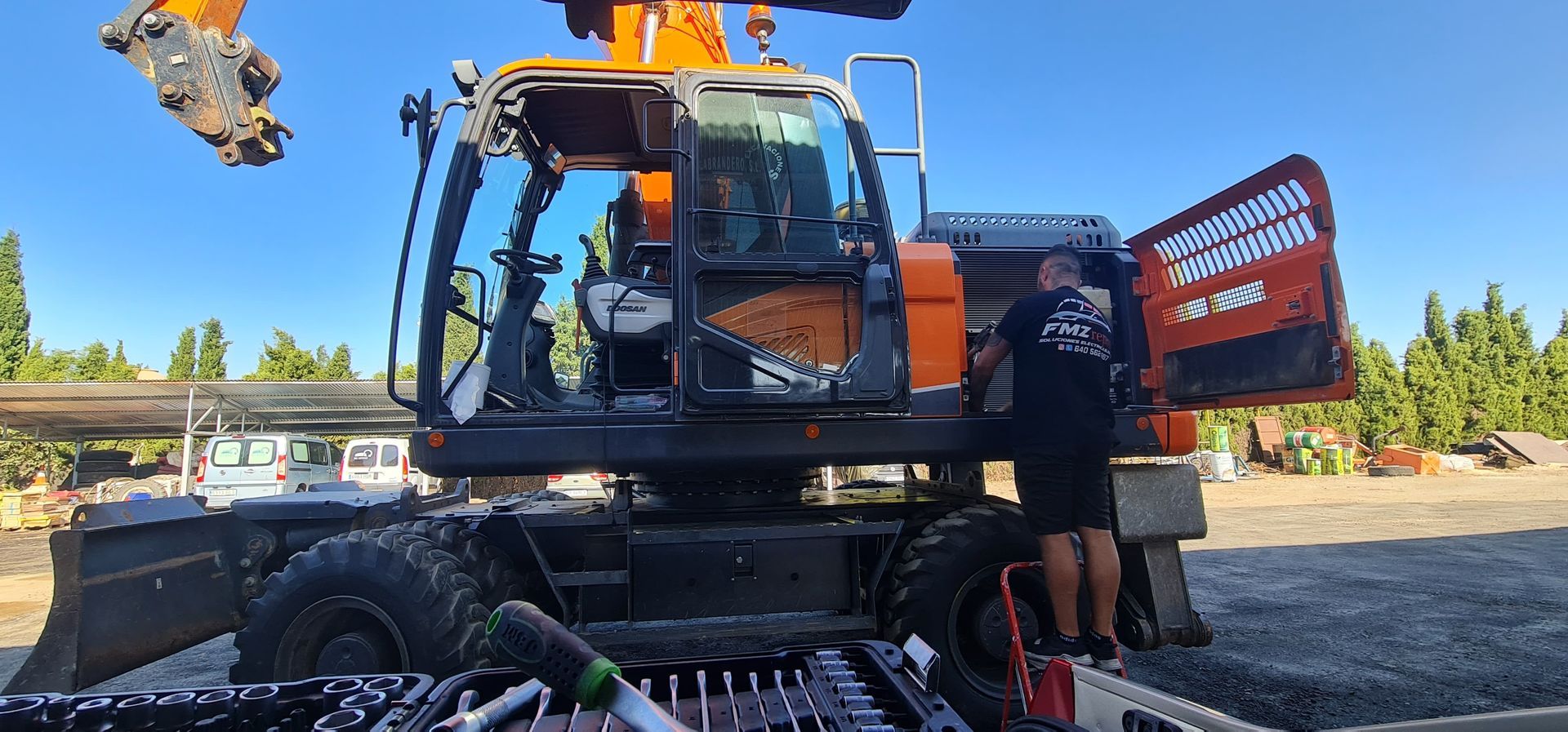 Un hombre está de pie junto a una gran excavadora naranja.