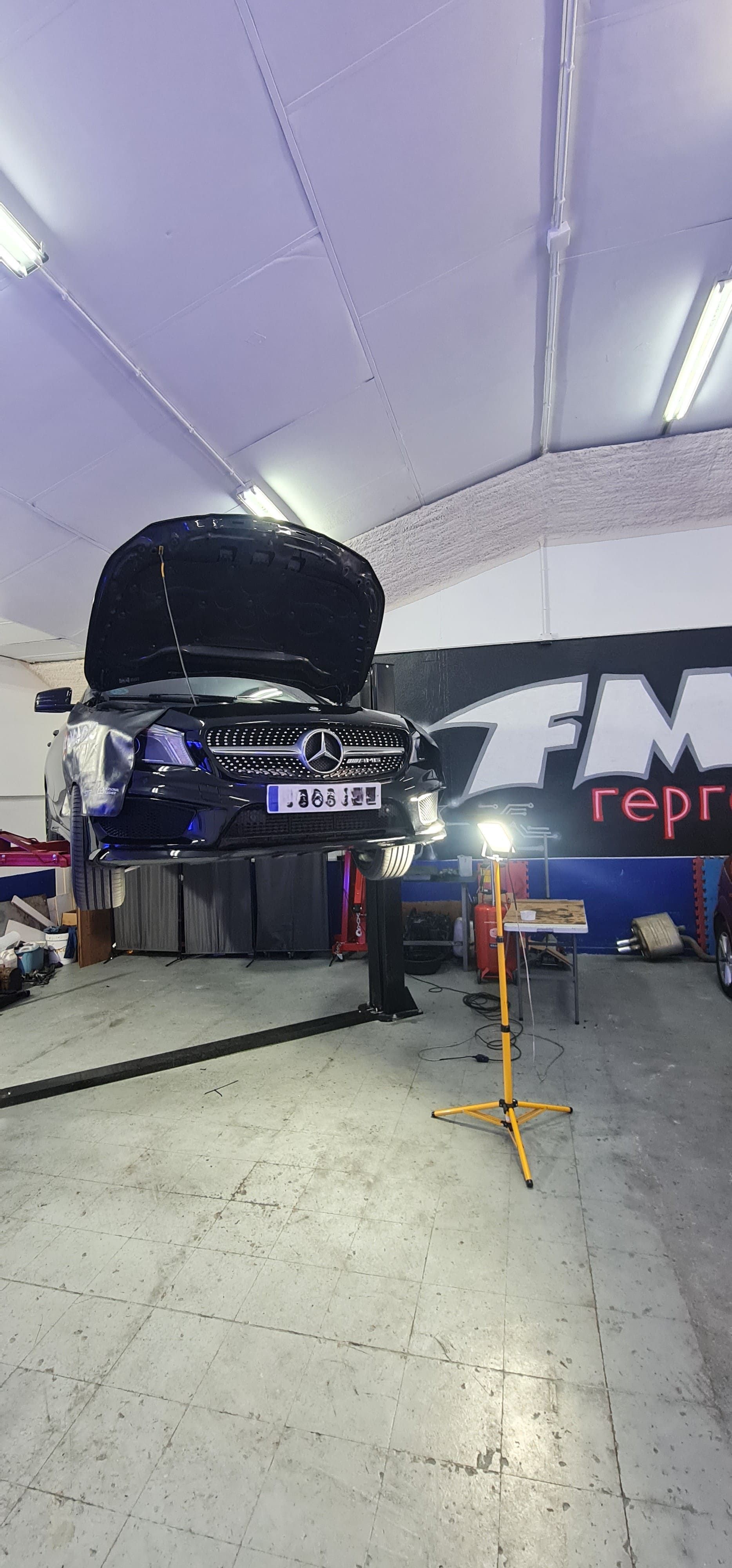 Se está reparando un coche en un garaje con el capó levantado.