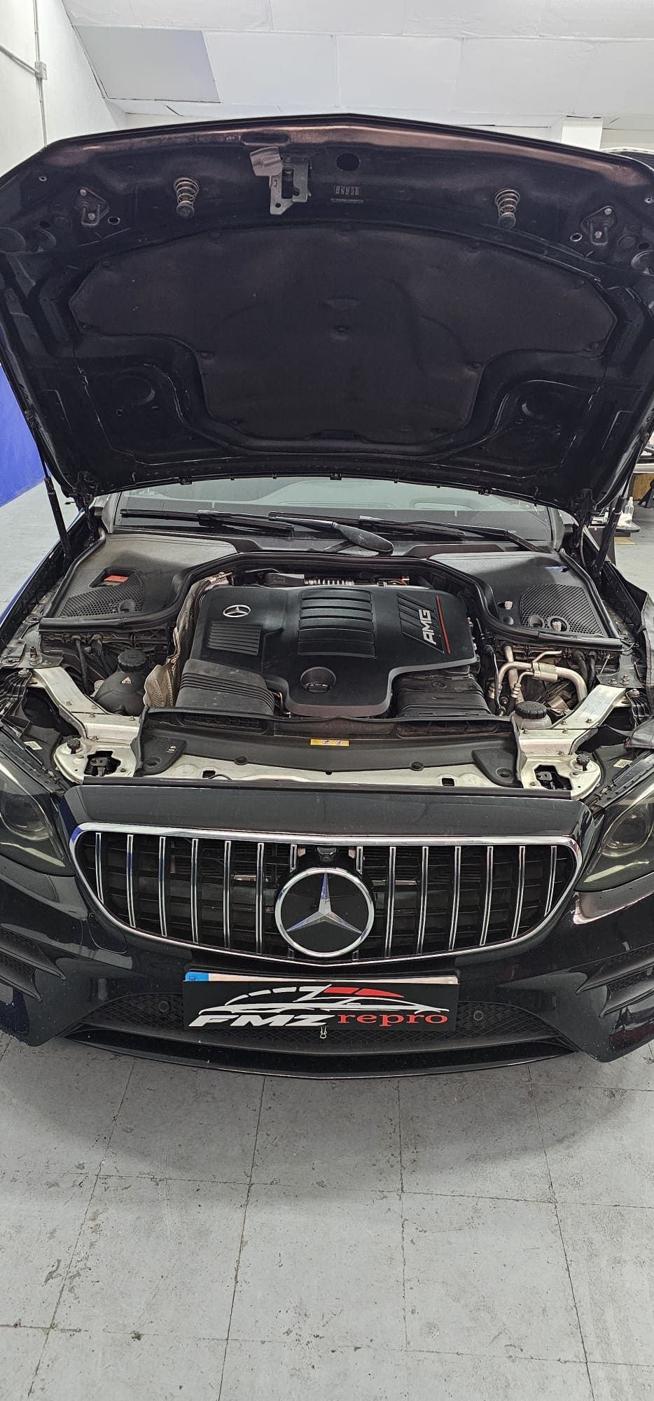 Un Mercedes Benz negro con el capó abierto en un garaje.