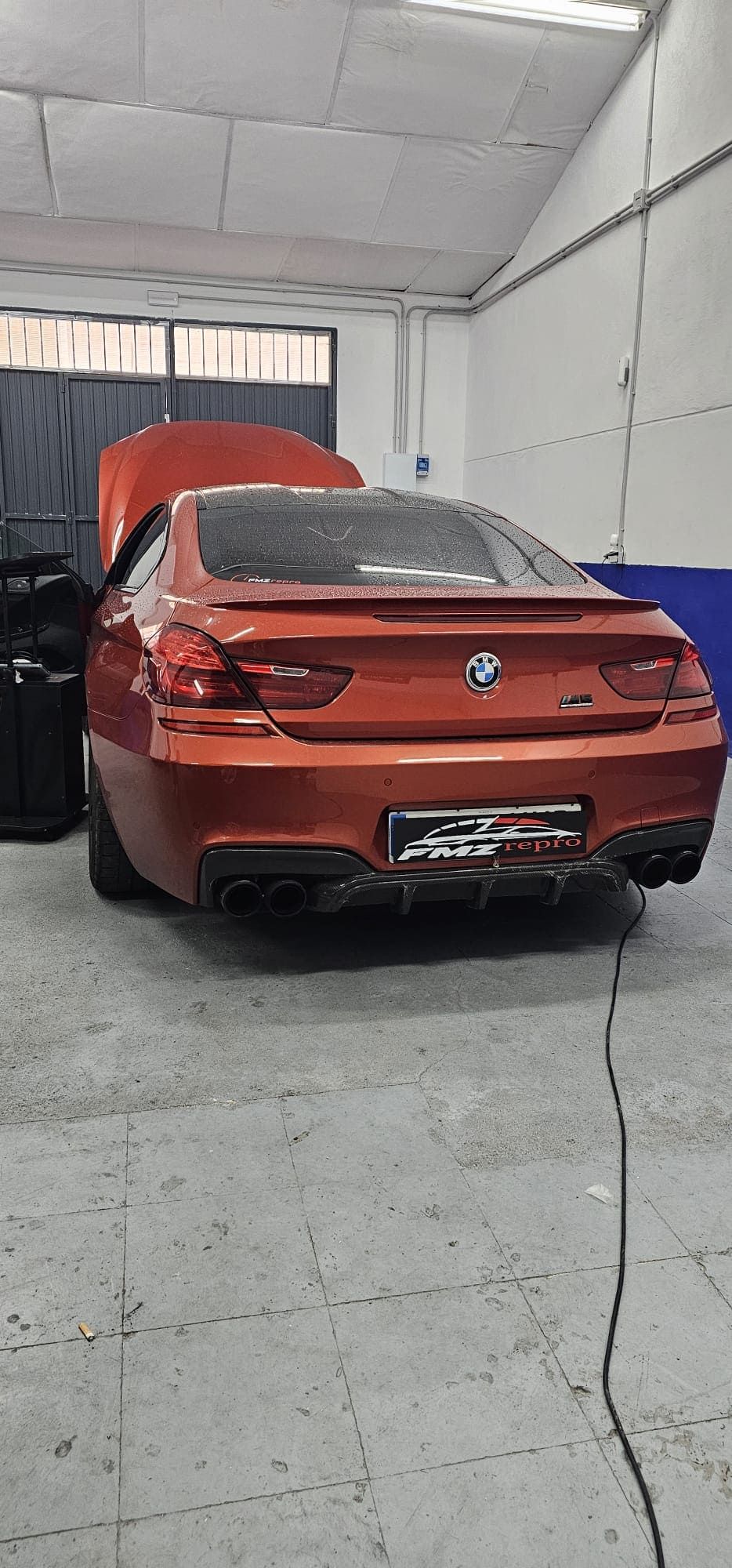 Un BMW rojo está aparcado en un garaje con el capó abierto.