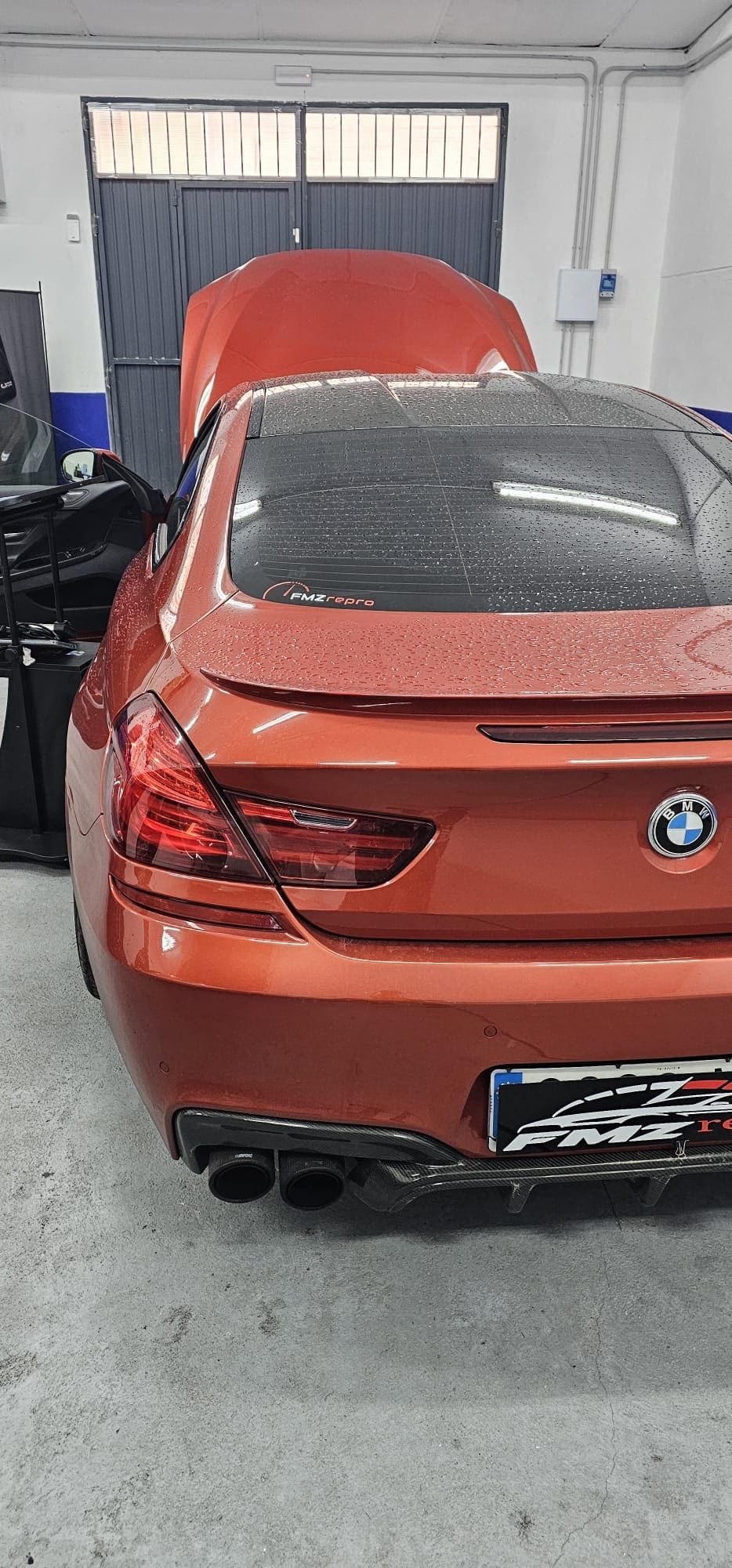 Un BMW rojo está aparcado en un garaje con el capó levantado.