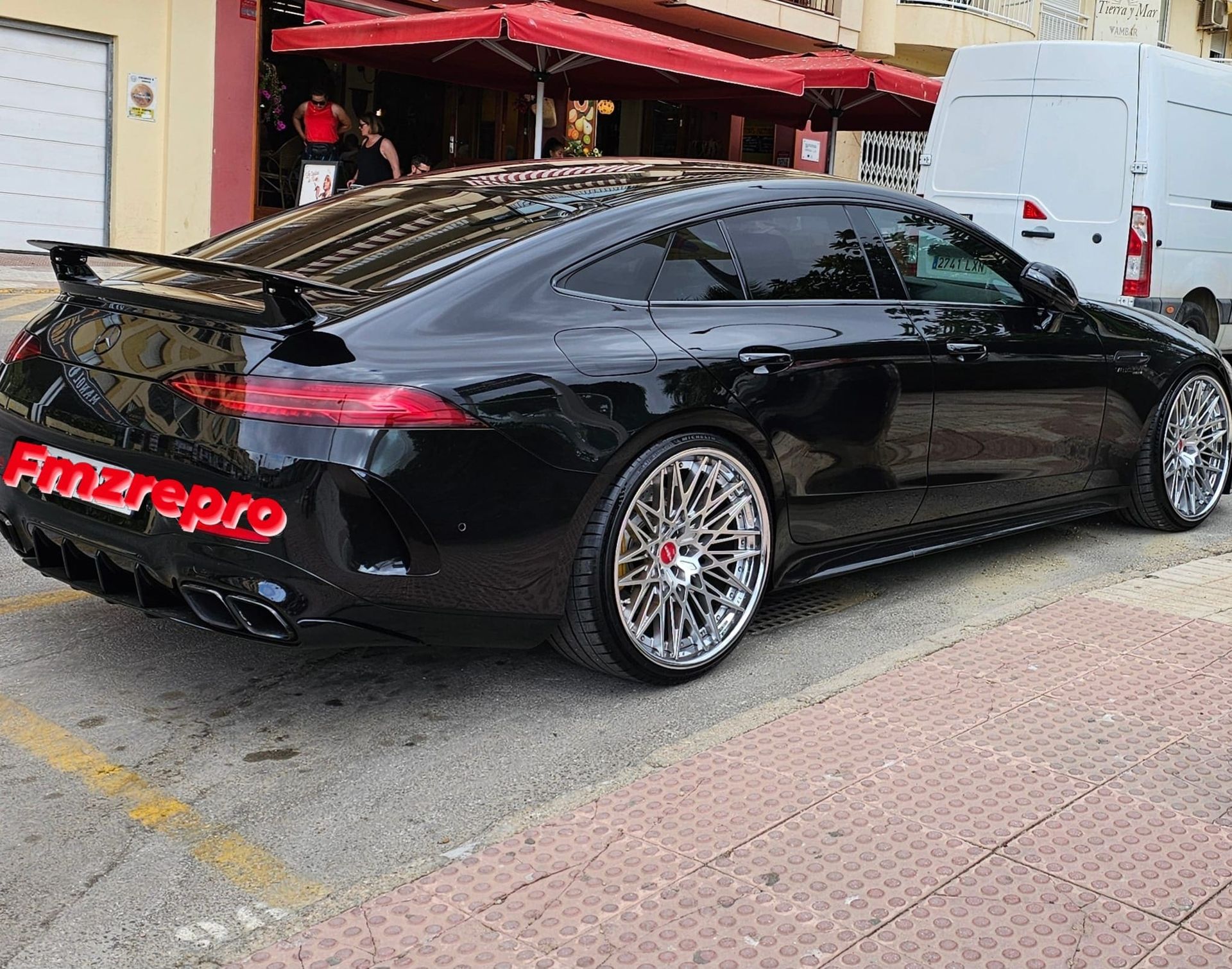 Un coche negro está aparcado al costado de la carretera frente a un restaurante.
