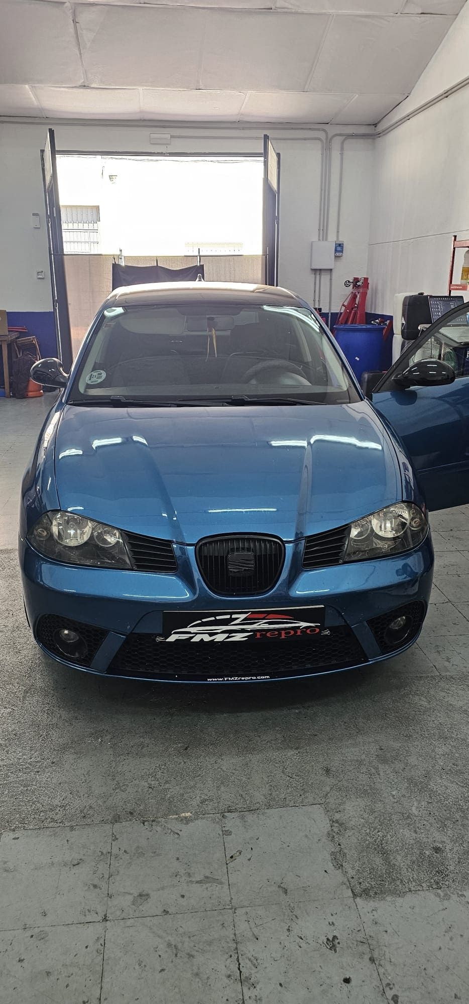 Un coche azul está aparcado en un garaje con las puertas abiertas.