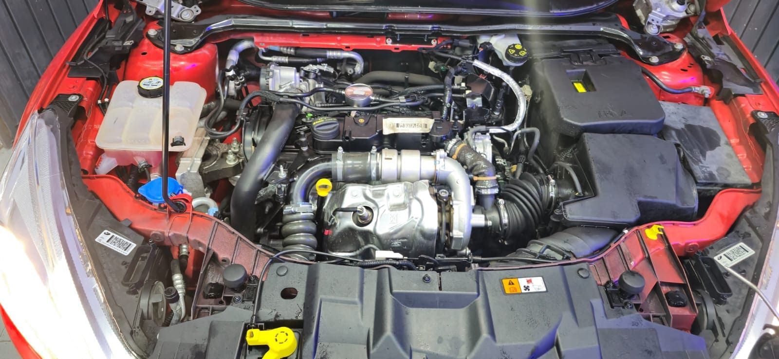 Se muestra el motor de un coche rojo con el capó abierto.