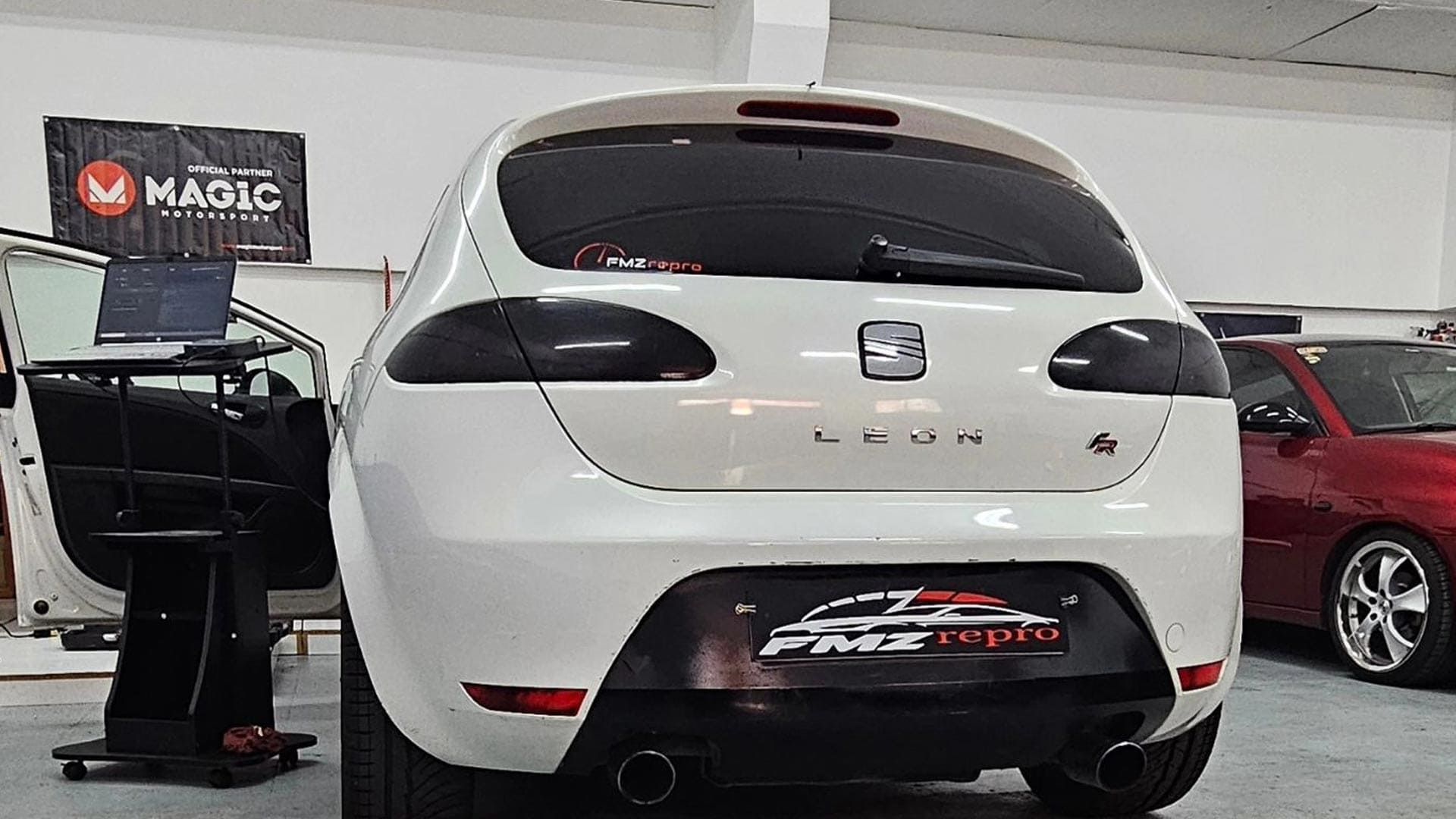 Un coche blanco está aparcado en un garaje al lado de un coche rojo.