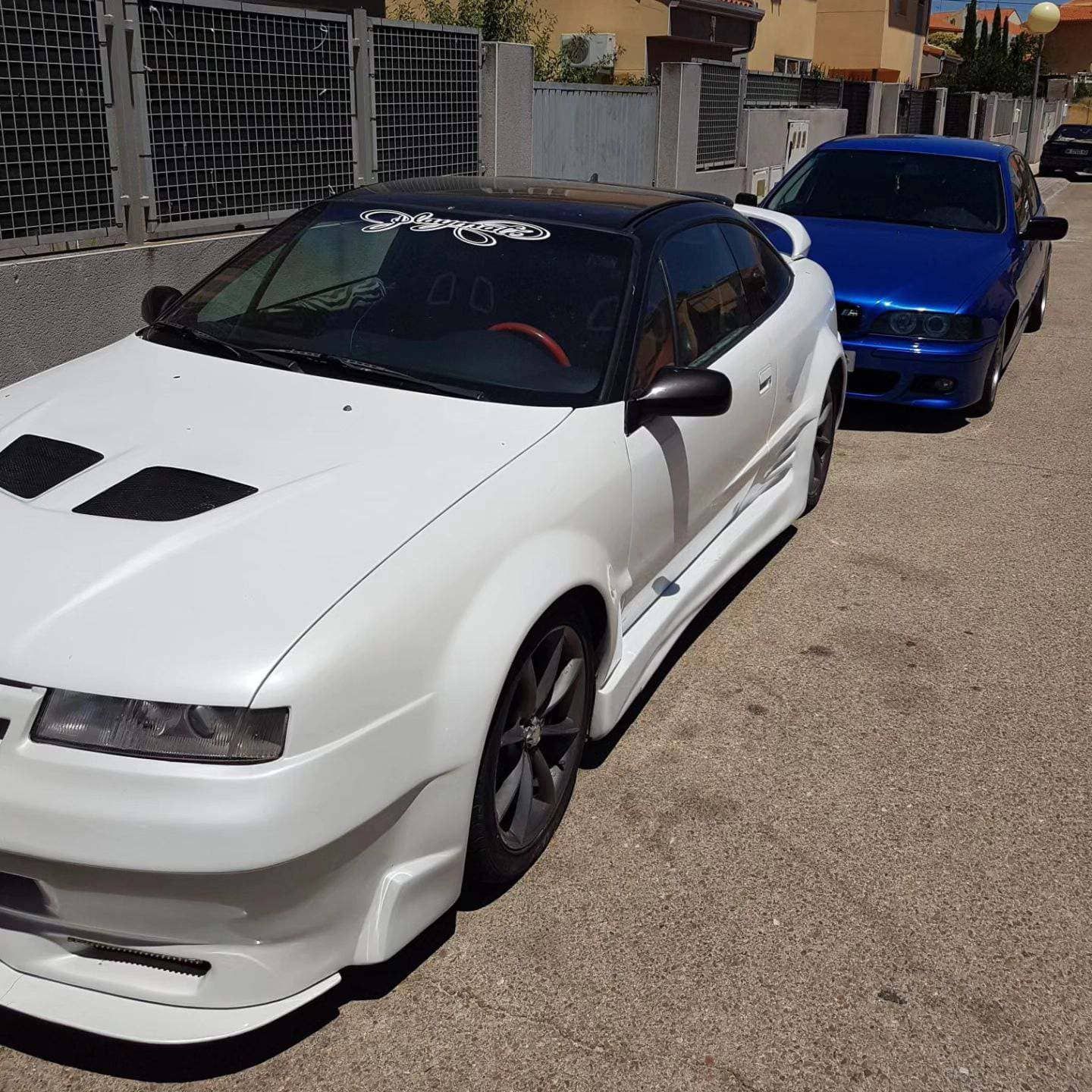 Un coche blanco está aparcado al lado de un coche azul.