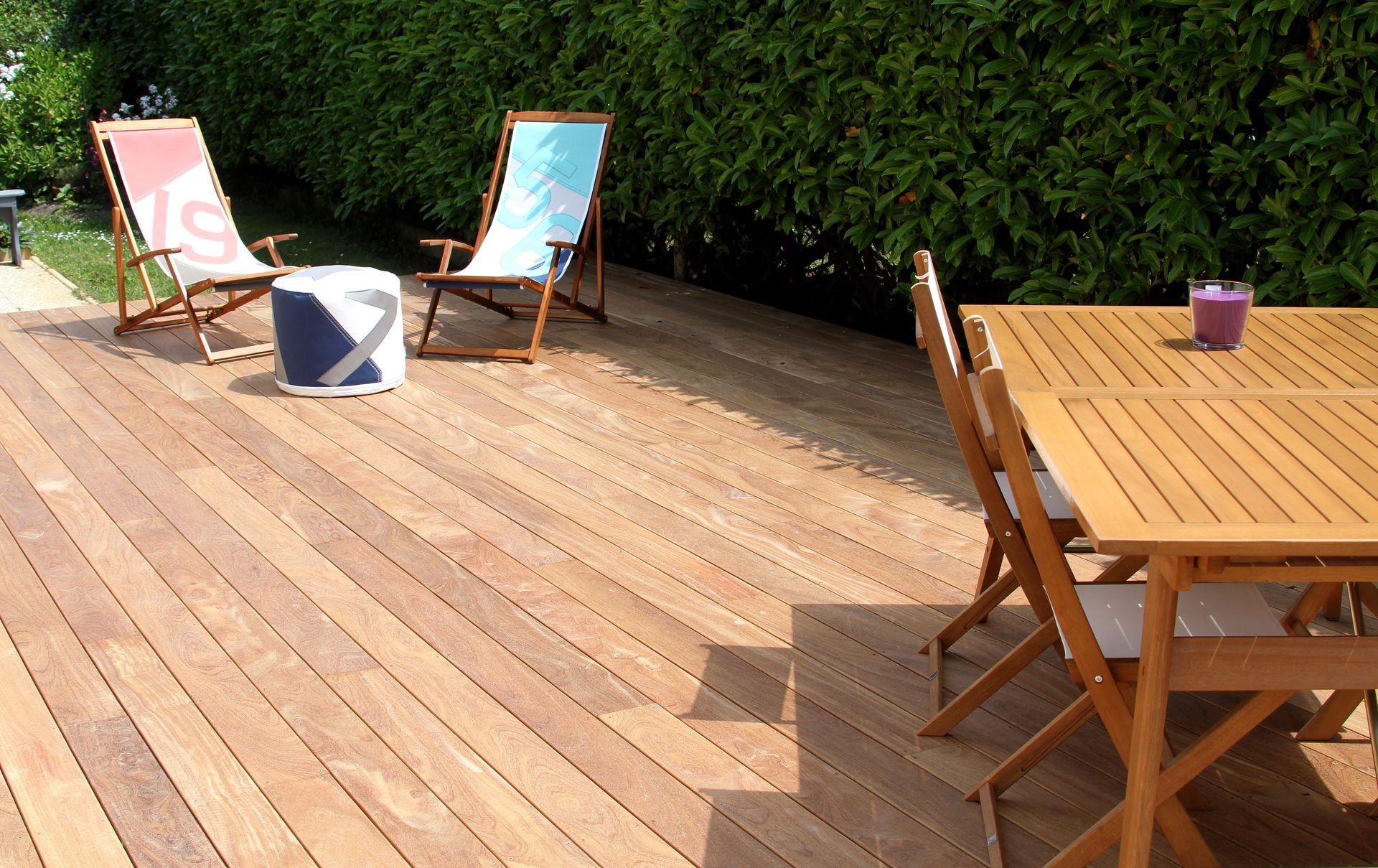 Terrasse en bois avec deux chaises longues, une table et des fleurs en pot baignées de soleil