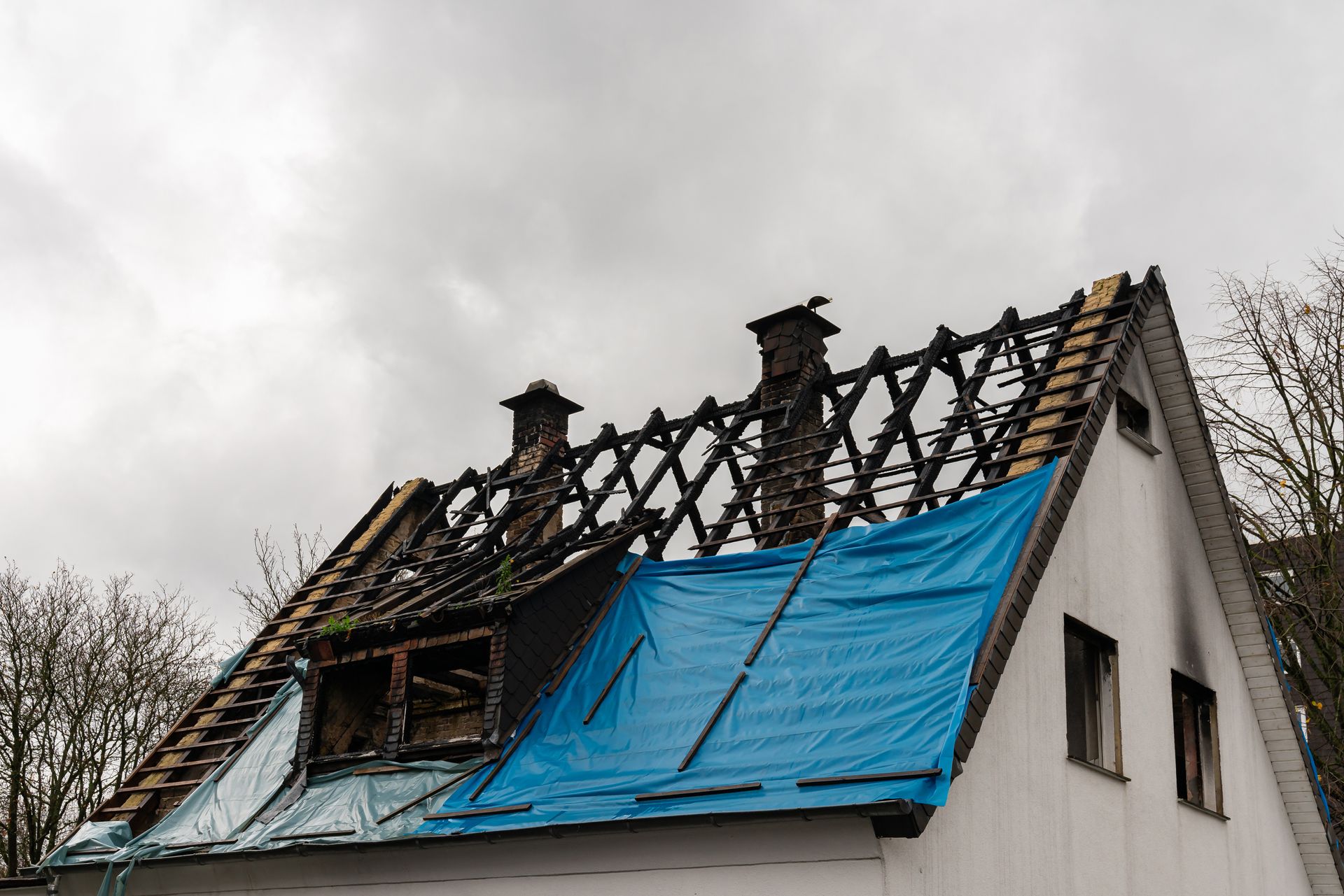 Toiture endommagée, chevrons calcinés et bâche bleue après l'incendie