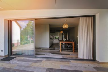 Ouvrez les portes coulissantes donnant sur une terrasse et une salle à manger intérieure avec une table et une suspension lumineuse.