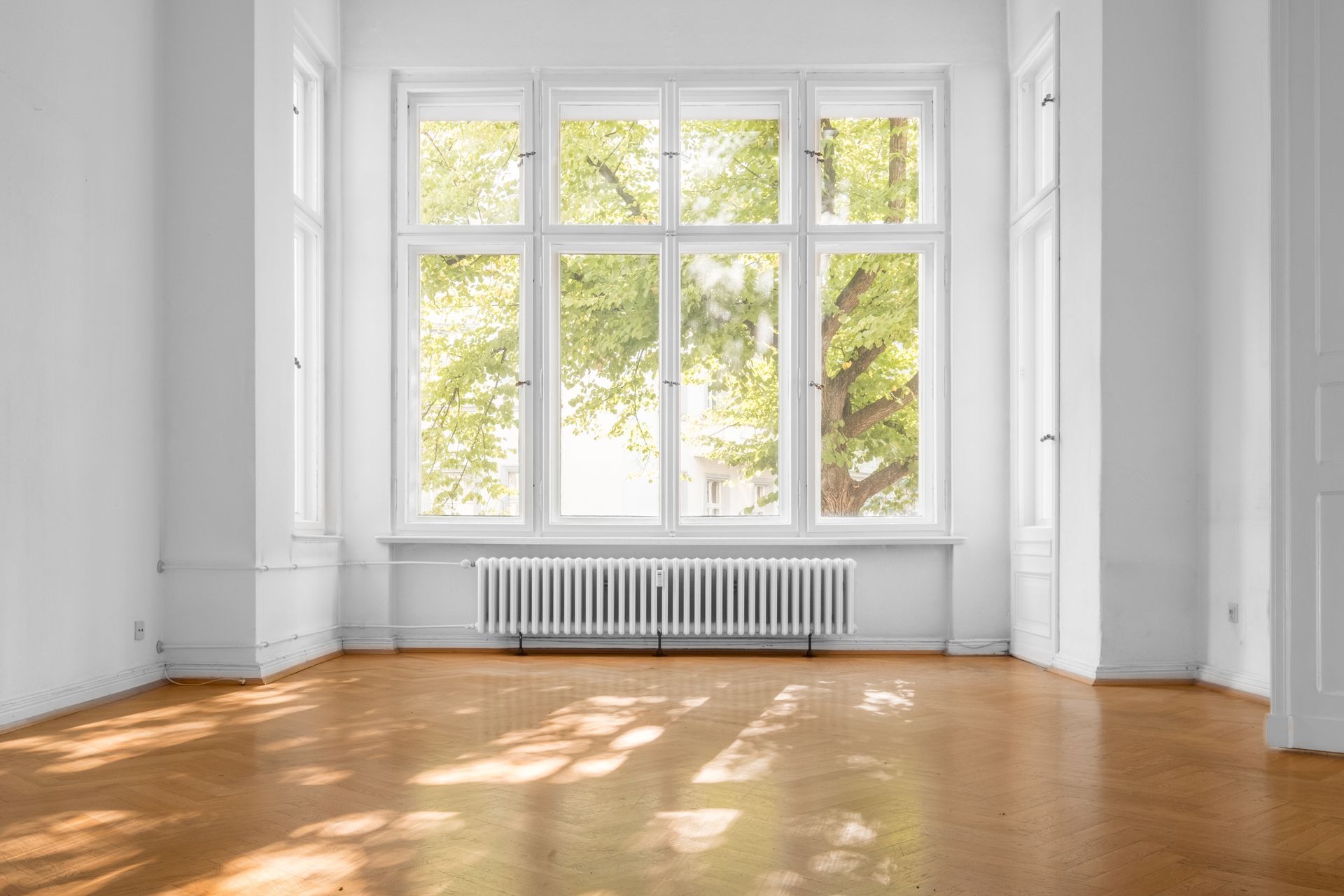 Pièce blanche vide avec de grandes fenêtres, la lumière du soleil sur le parquet et un radiateur sous les fenêtres.