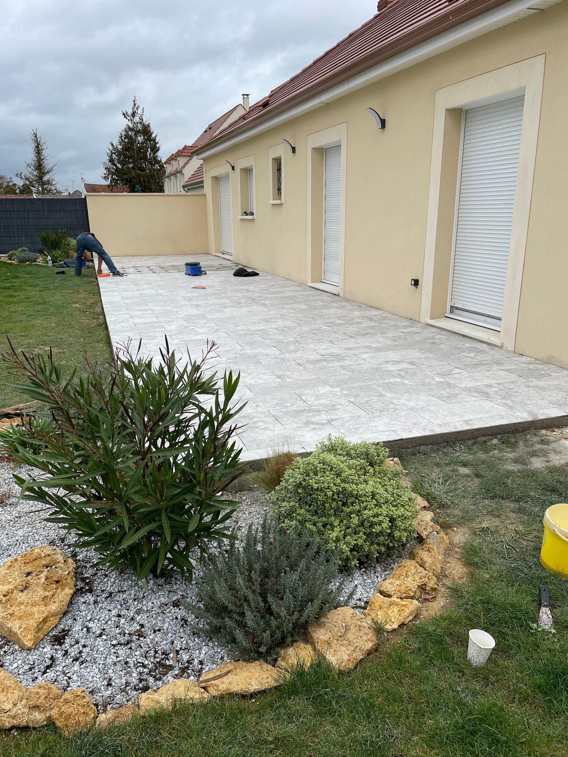 Terrasse arrière avec pavés blancs à côté d'une maison beige et d'un parterre de gravier aménagé.