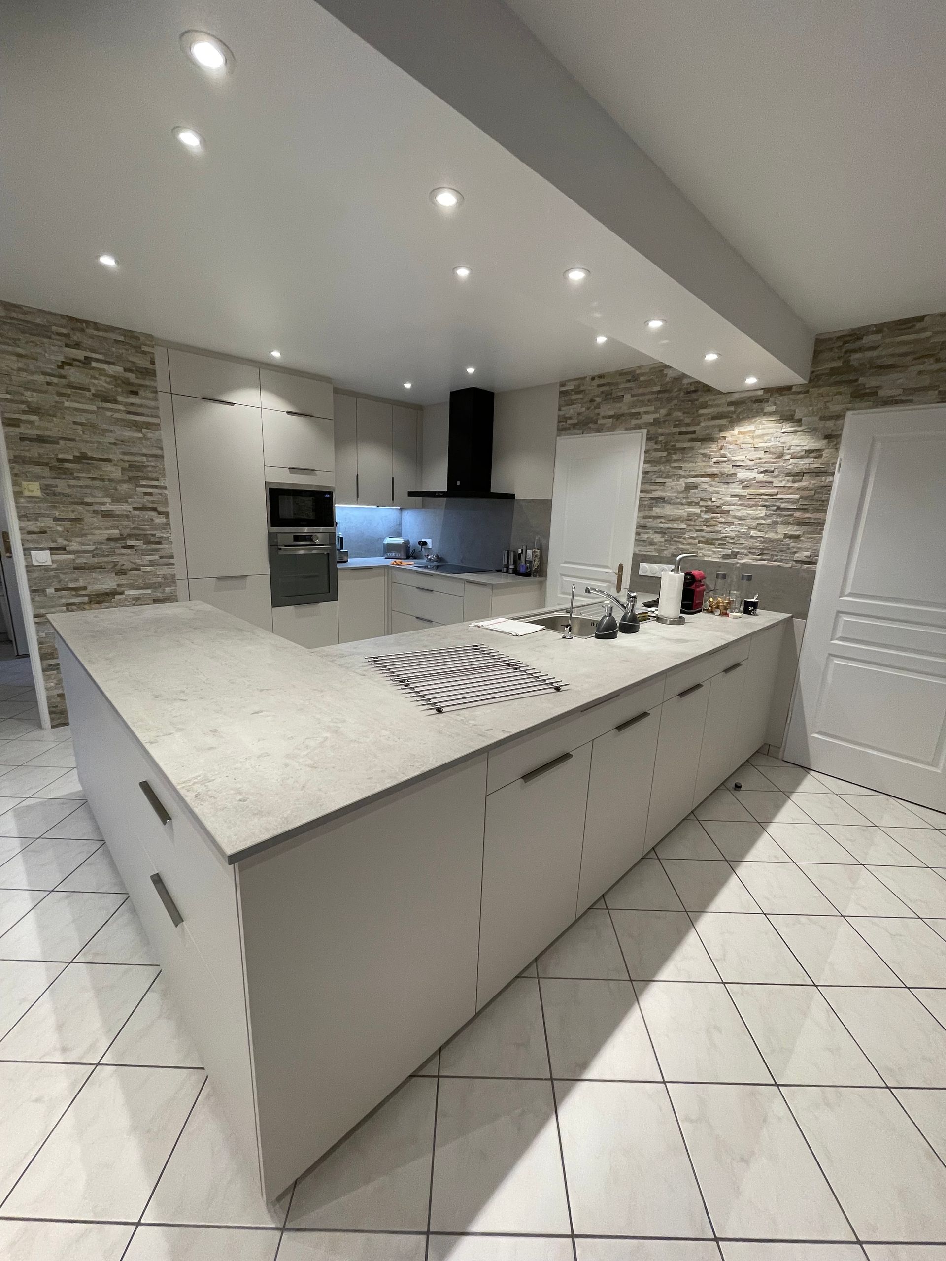 Cuisine et salle à manger ouvertes avec îlot central foncé, suspensions lumineuses et parquet.