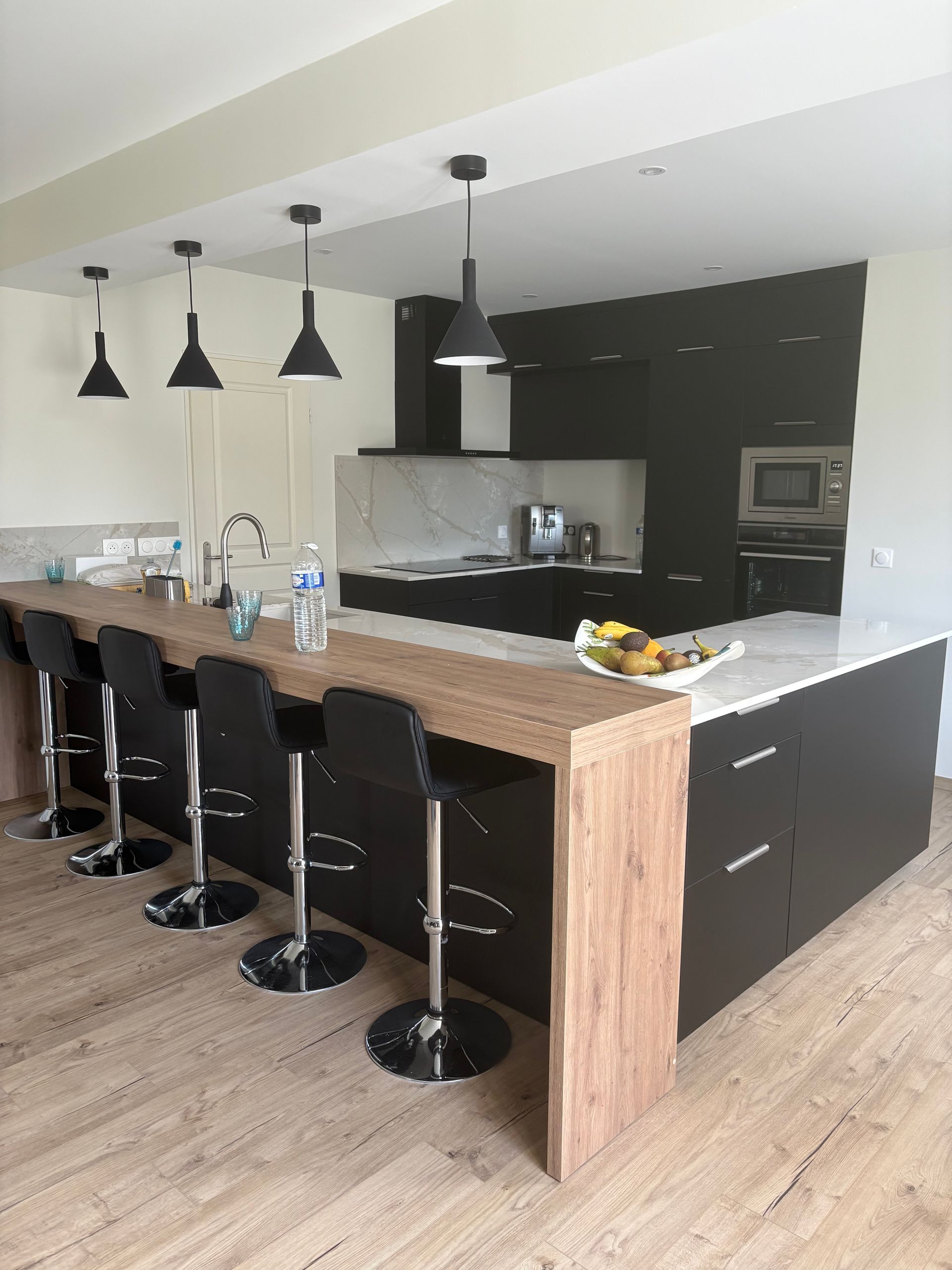 Cuisine moderne avec un grand îlot central, des tabourets de bar noirs, des suspensions lumineuses et un parquet clair.