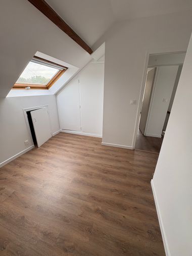 Grenier blanc vide avec puits de lumière incliné, parquet et placard intégré.