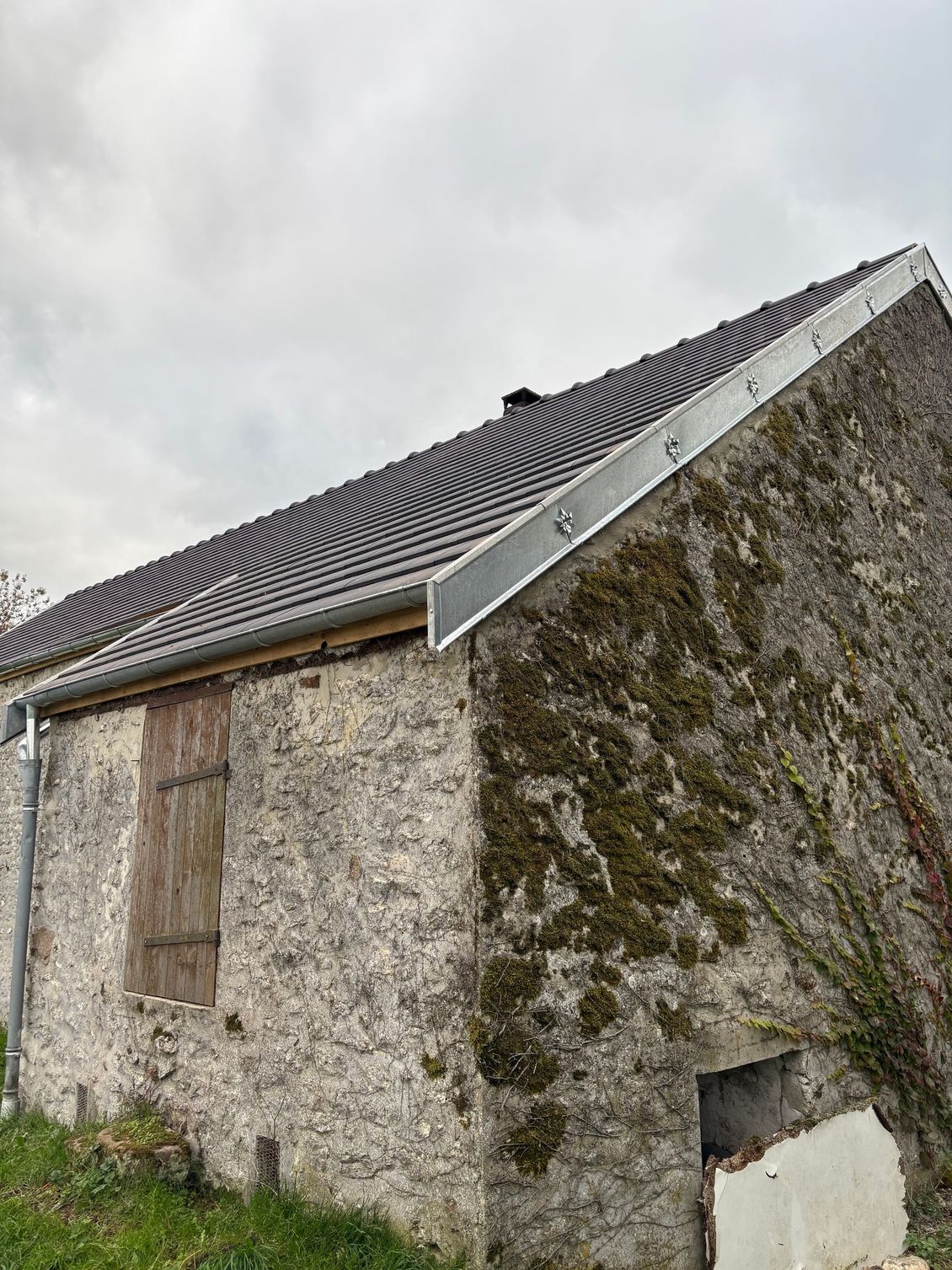 Vieille maison en pierre avec un mur couvert de mousse et un toit de tuiles sombres sous un ciel nuageux