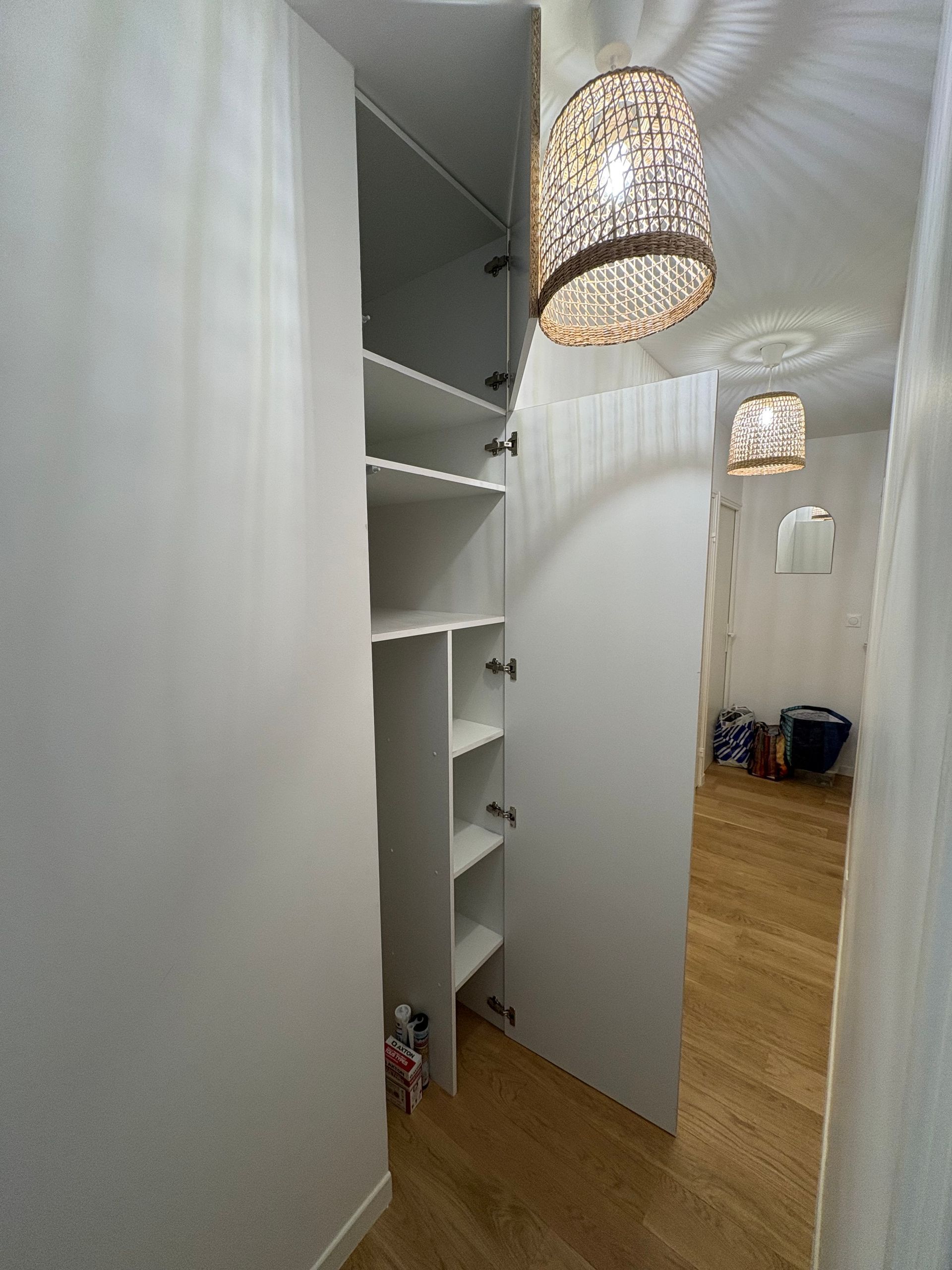 Placard blanc dans le couloir avec étagères intégrées, parquet et suspension lumineuse en tissu tressé.