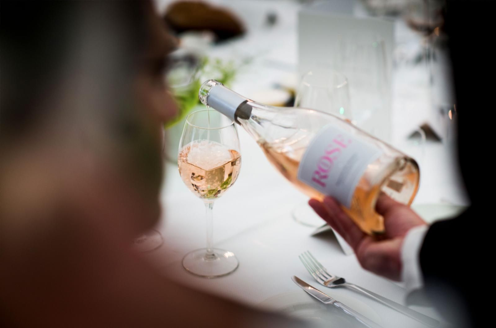 Eine Person schenkt Roséwein in ein Glas an einem gedeckten Tisch ein.