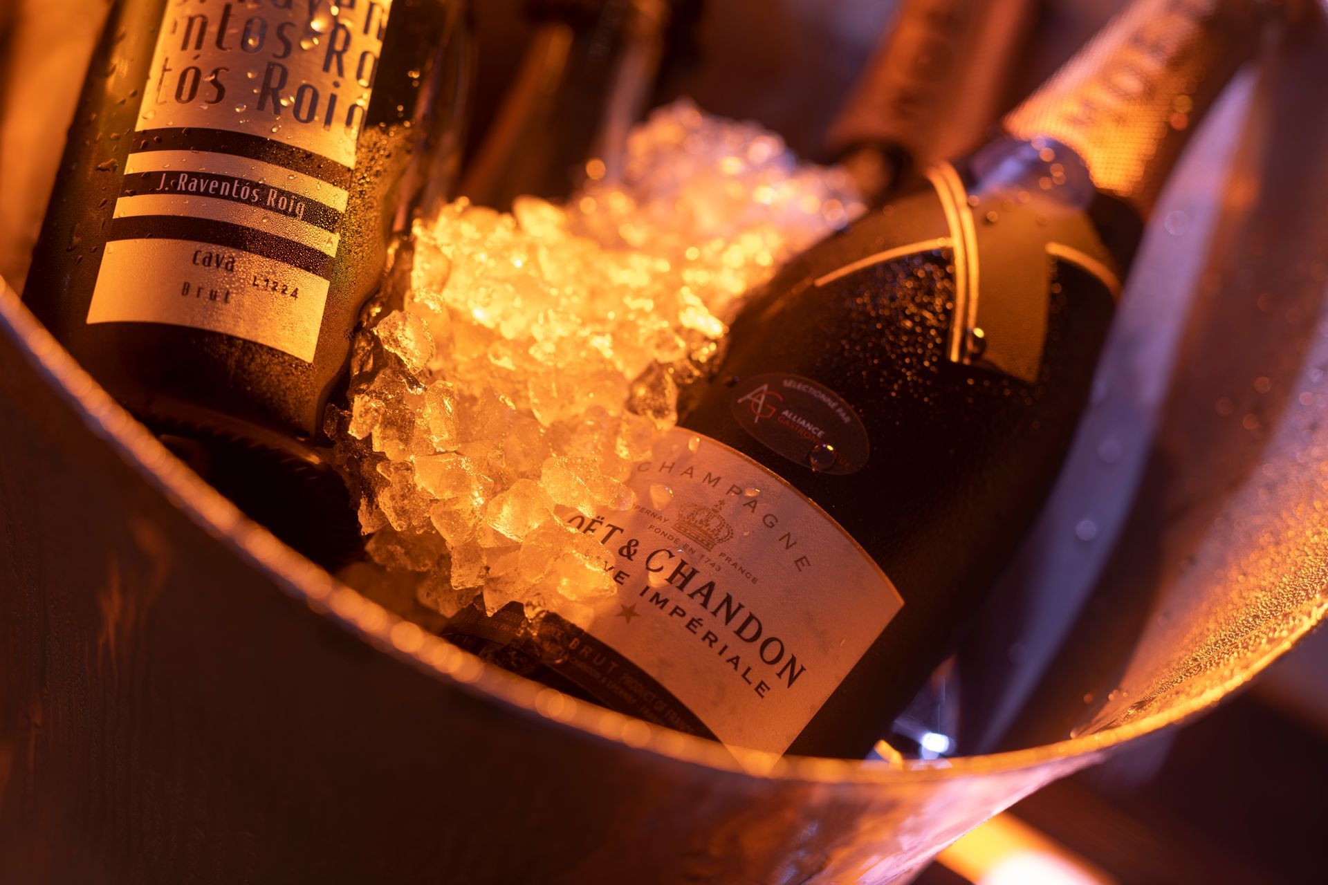 Champagneflessen in een metalen ijsemmer, verlicht met warm licht.