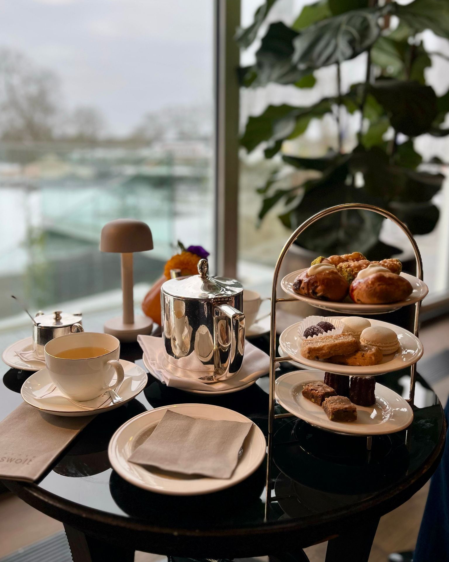 Nachmittagstee auf einem Tisch am Fenster; Etagere mit Gebäck, silberne Teekanne und Tasse.
