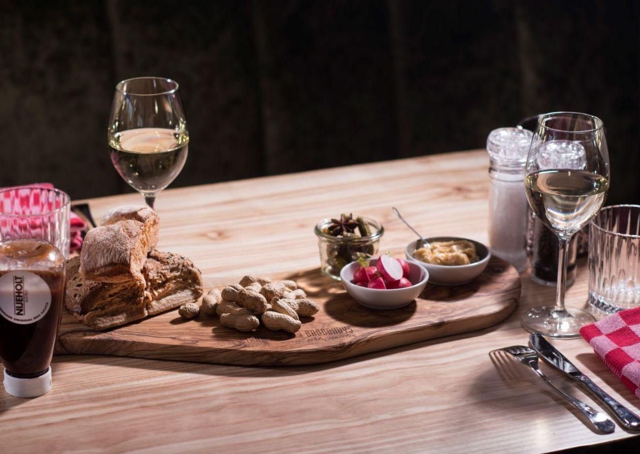 Ein Holztisch mit Brot, Dips, Weingläsern und Salz-/Pfefferstreuern in einem schummrigen Restaurant.