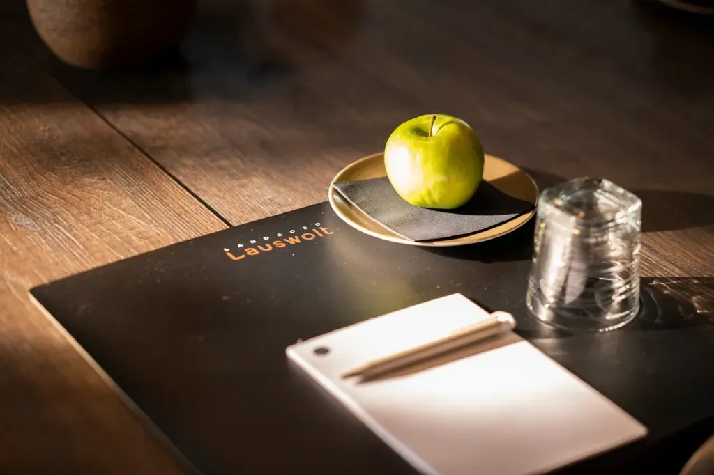 Groene appel op een klein bordje, notitieblok en glas water op een donker bureau.