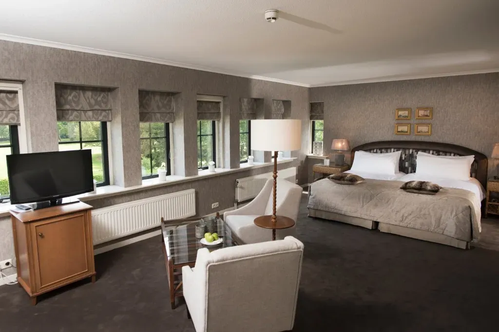 Hotelkamer met een groot bed, een zithoek, een tv en ramen met uitzicht op een groen landschap.