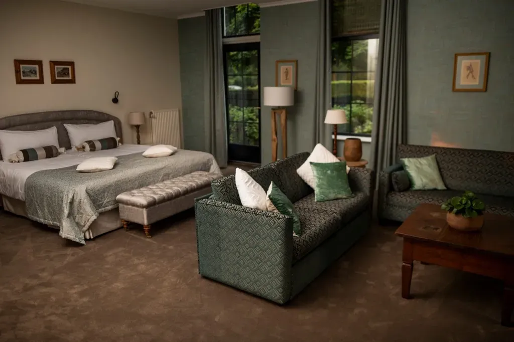 Ruime hotelkamer met kingsize bed, twee banken en donkergroene gordijnen.